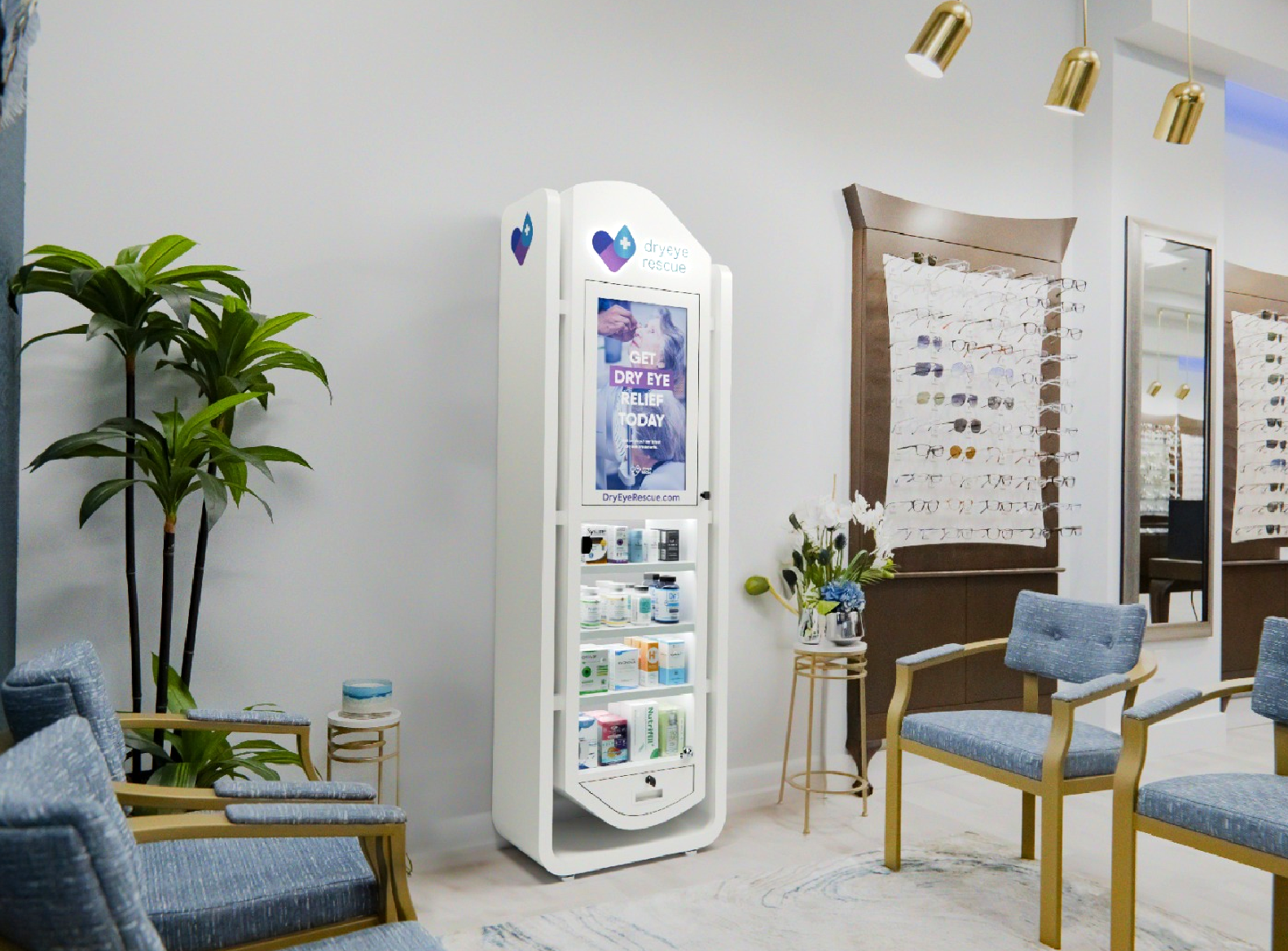 A modern optometry office features blue cushioned chairs and a sleek white DryEye Rescue vending machine with eye care essentials. A Slim tower display of eyeglasses optimizes space under gold pendant lights, next to a lush plant.