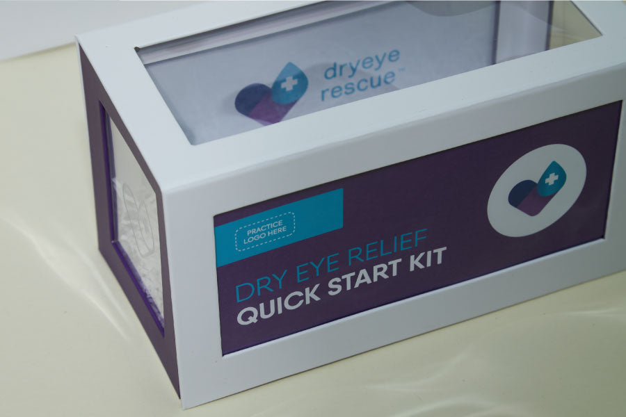 A white rectangular box labeled Dry Eye Relief Quick Start Kit with purple and turquoise accents. The box features a logo with a purple heart and a turquoise cross. The lid is transparent, revealing a folded fabric inside.