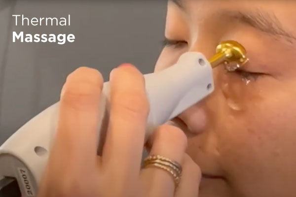 A person is receiving a thermal massage near their eye using a specialized device with a gold-tipped head. Their eyes are closed, and they are wearing rings. Text on the image reads Thermal Massage.