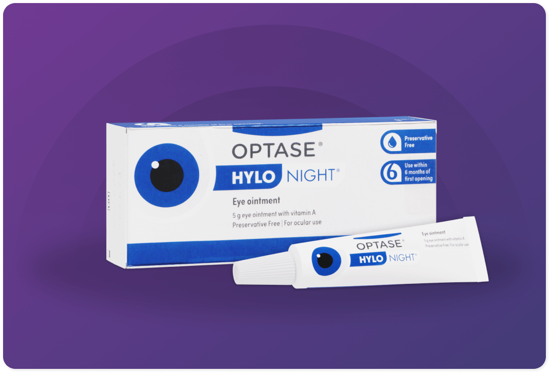 Box and tube of Optase Hylo Night eye ointment on a purple background. The packaging includes a large eye graphic, and text indicating it is preservative-free, contains vitamin A, and should be used within six months of opening.