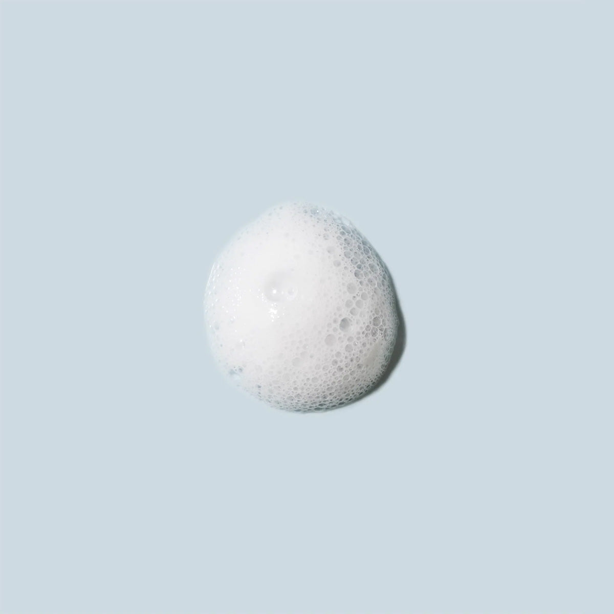 A circular cluster of white soap bubbles on a light blue background, resembling a small puff of foam, evokes the essence of the Daily Practice Purifying Foam Cleanser—Gentle & Hydrating for Eyes & Lashes (80mL).