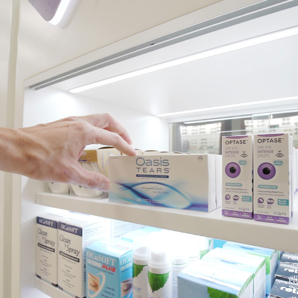 A hand reaches for a box from the DryEye Rescue Free Standing Floor Display Free Rent (Large), illuminated by a digital screen highlighting its benefits amidst perfectly arranged Optase boxes and other eye care products, resembling a smoothly operating revenue-generating machine.