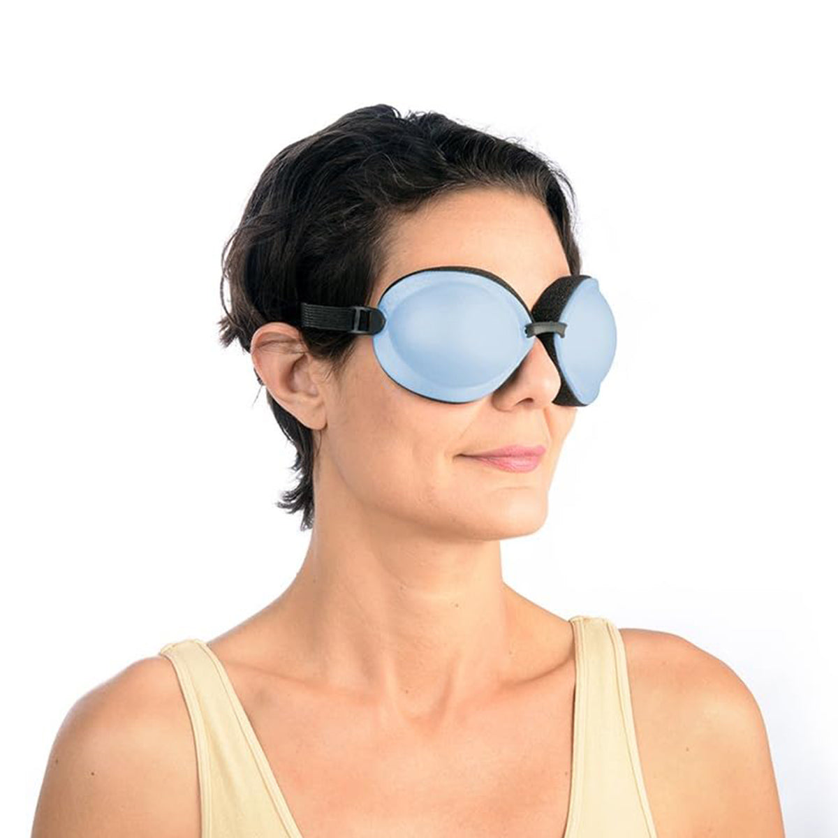 Wearing oversized Tranquileyes XL goggles by PRN, in light blue with a black strap, and a cream tank top, the person with short dark hair gazes left against a white background, embodying calmness through advanced moist-heat therapy for severe dry eye and MGD.