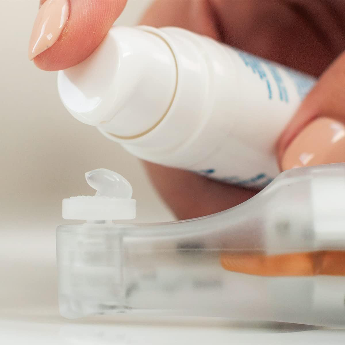 A close-up shows a neatly manicured hand pressing a white NuLids All Natural At-home Eye Treatment device by Nusight Medical to dispense dry eye treatment onto a clear plastic surface.