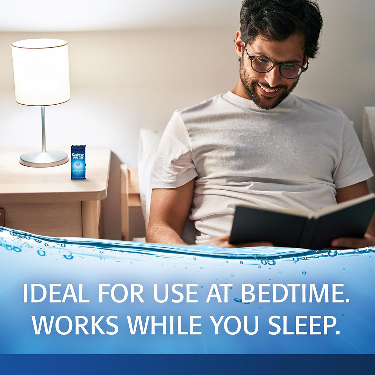 A man with glasses sits in bed reading and smiling. A small box of Vicks NyQuil and Refresh Lacri-Lube Lubricant Eye Ointment for Nighttime dryness (3.5g Tube) by Abbvie rests on the bedside table by a lamp. The text reads, Ideal for use at bedtime. Works while you sleep.