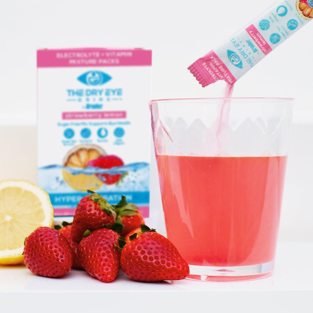 A glass of pink beverage with fresh strawberries and a lemon slice is enhanced as a sachet from Bruders Dry Eye Drink™ Daytime—Doctor-Formulated Electrolyte Hydration for Eye Health (Strawberry Lemonade, 20 Packets) is poured in, subtly promising eye health benefits and dry eye relief.