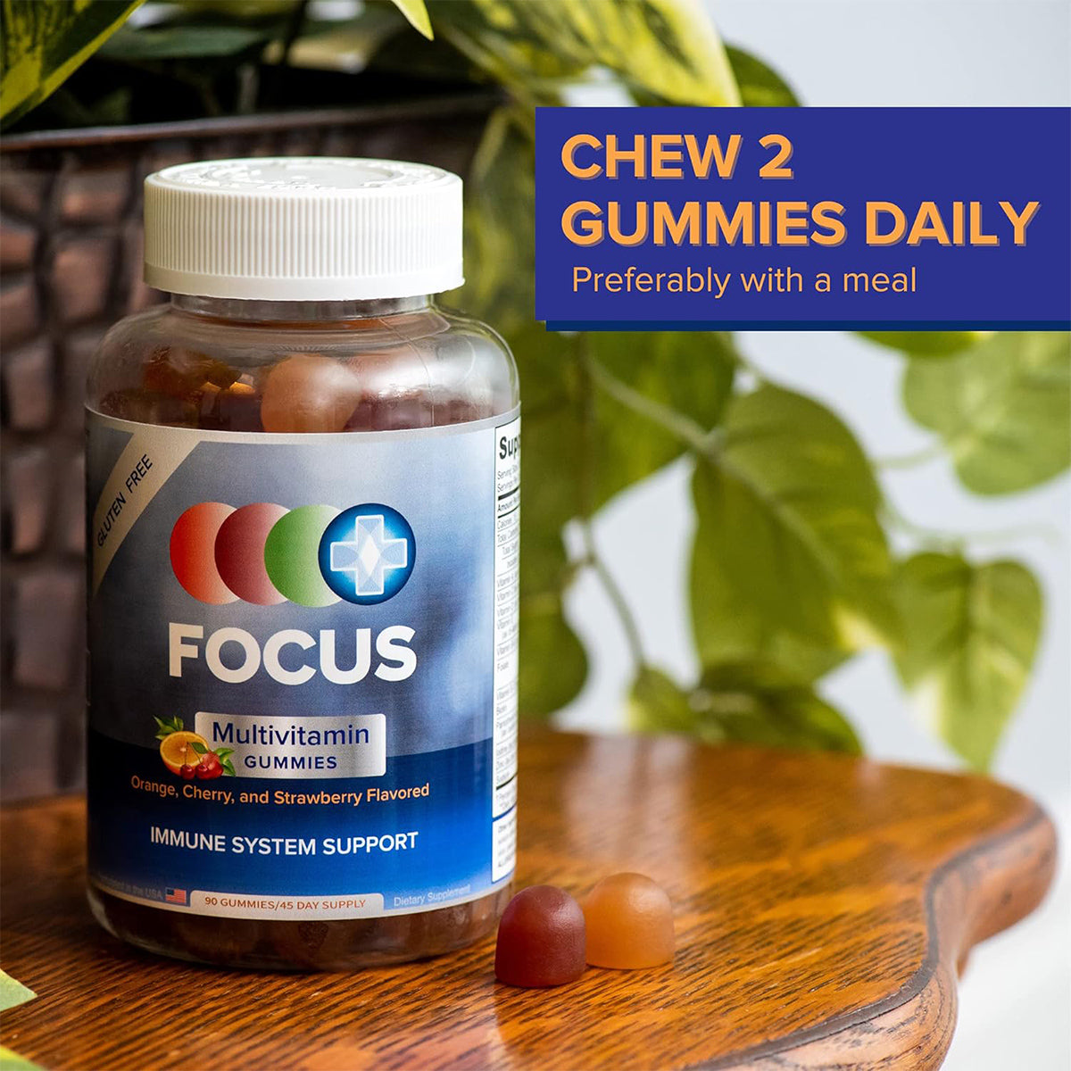 A bottle of Focus Multivitamin Gummies by Focus Vitamins, featuring orange, cherry, and strawberry flavors, is on a wooden table with green plants in the background. A text box says, Chew 2 Gummies Daily for essential nutrients and immune health, preferably with a meal.