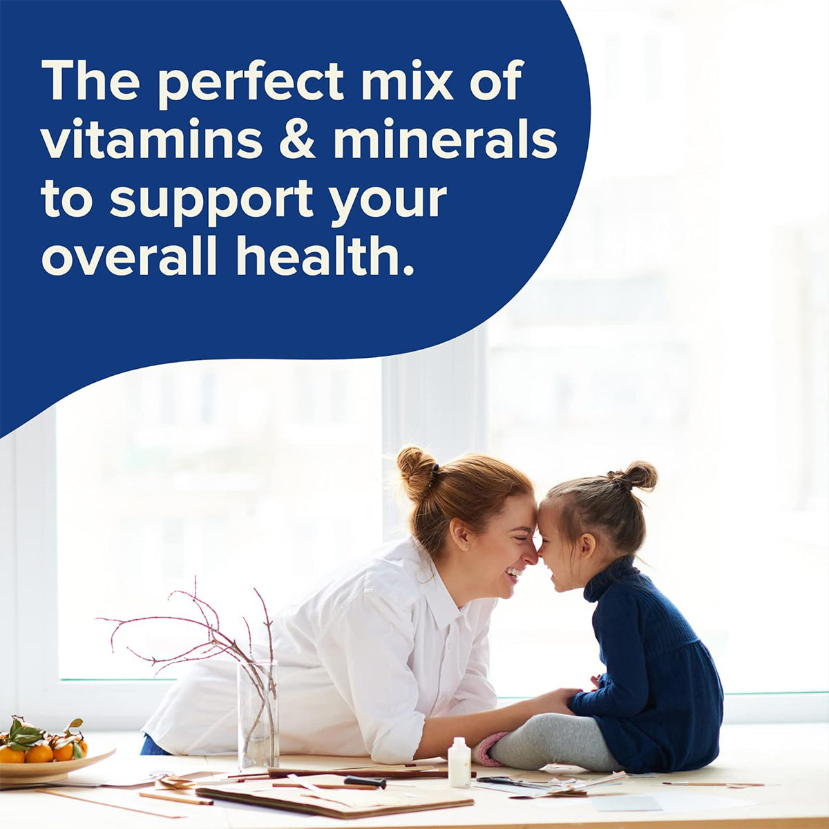 A woman and young girl smile, touching noses by a window next to a desk with papers, a plant, and fruits. Text reads: Focus Vitamins offers the perfect mix of multivitamin gummies to support your overall health.