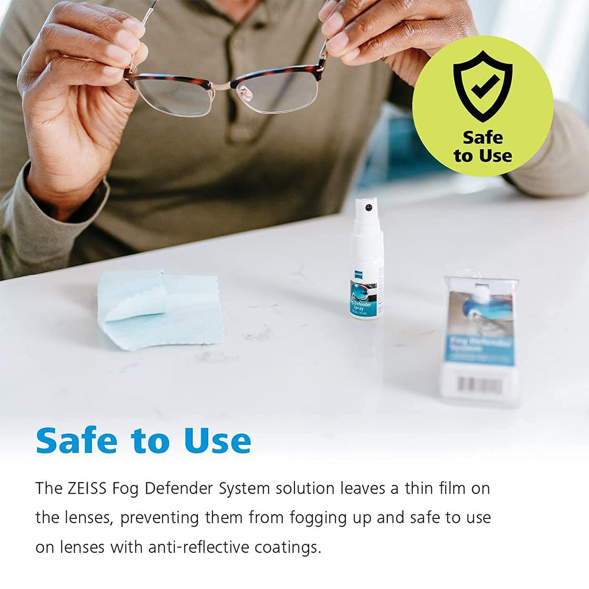 A person carefully uses the ZEISS Fog Defender System Anti-Fog Spray for Glasses, featuring a spray bottle and microfiber cloth. A green badge with a shield icon that reads Safe to Use rests on the table, ensuring your lenses remain fog-free.