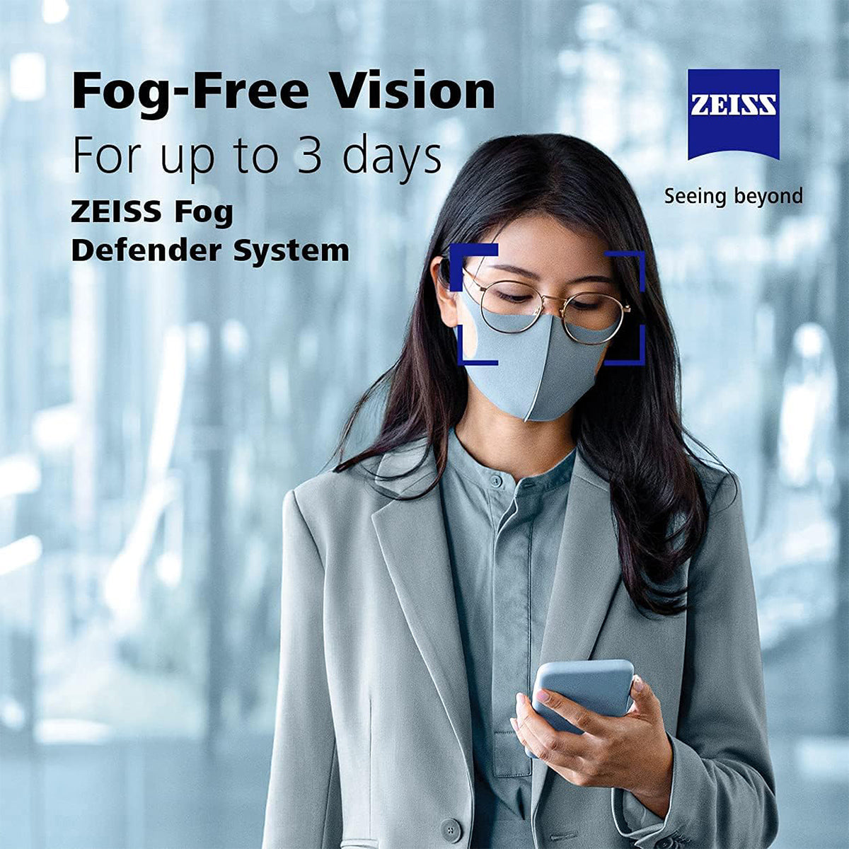In a stylishly blurred scene, an individual in a gray suit uses their smartphone while wearing glasses and a face mask. They demonstrate the ZEISS Fog Defender System Anti-Fog Spray for Glasses, showcasing fog-free vision for up to 3 days with just one spray and microfiber cloth.