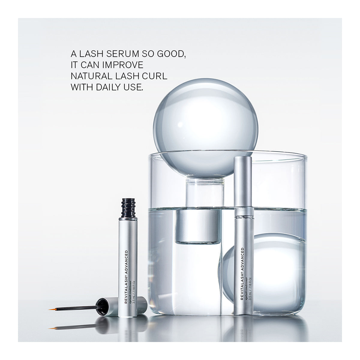 A minimalist ad presents RevitaLash Advanced PRO Eyelash Conditioner and Enhancing Serum in sleek silver packaging, with two bottles on glass spheres and cylinders. Text reads: A LASH SERUM SO GOOD, IT CAN IMPROVE NATURAL LASH CURL WITH DAILY USE. Discover the lash-enhancing formula today.