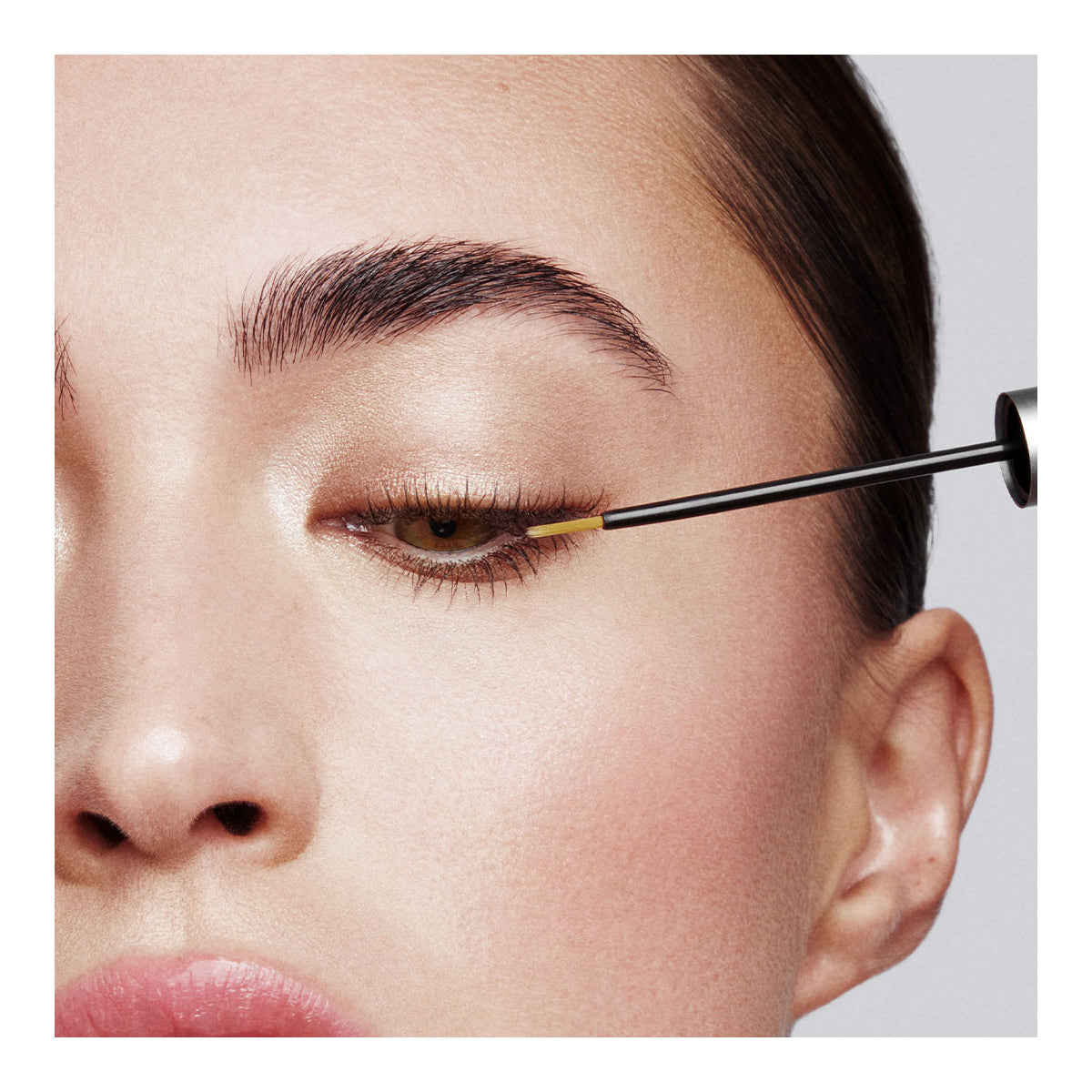Close-up of someone applying eyeliner with precision, enhancing a natural makeup look. Their well-defined eyebrows and lashes are conditioned with RevitaLash Advanced PRO Eyelash Conditioner and Enhancing Serum by RevitaLash, set against a neutral background.