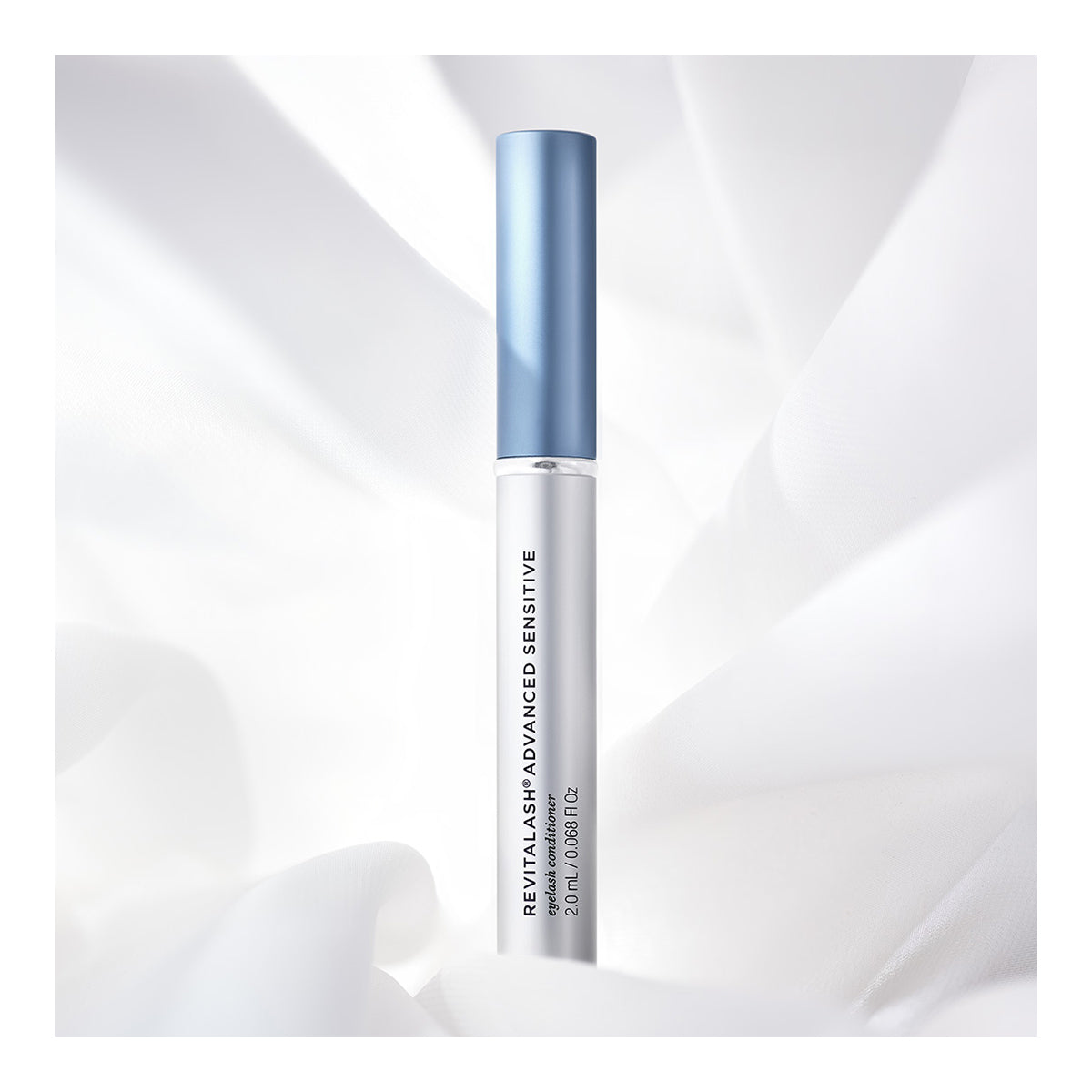 A 2.0mL tube of RevitaLash Advanced Eyelash Conditioner and Enhancing Serum Sensitive, with Revitasome Technology, showcases a sleek silver body and blue cap against a backdrop of soft white fabric.