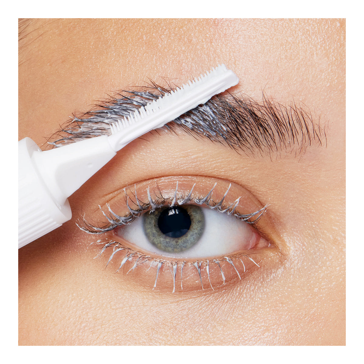 A close-up of an eye with silver mascara on the lashes shows a white applicator brushing through the brow. RevitaLash Lash and Brow Masque enhances shine for healthy lashes and brows against smooth, well-lit skin, accentuating the eyes striking details.