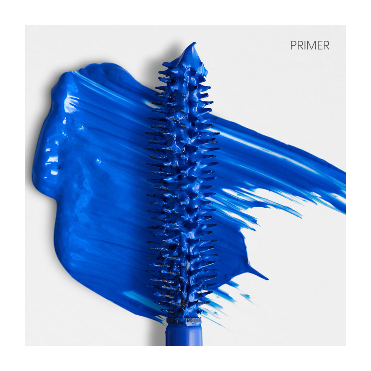 A close-up of the RevitaLash Double-Ended 2-in-1 Lash Primer & Mascara Volume Set wand shows vibrant blue mascara smeared on a white background. PRIMER appears in the upper right corner, highlighting short bristles coated with vivid blue for a dramatic look.