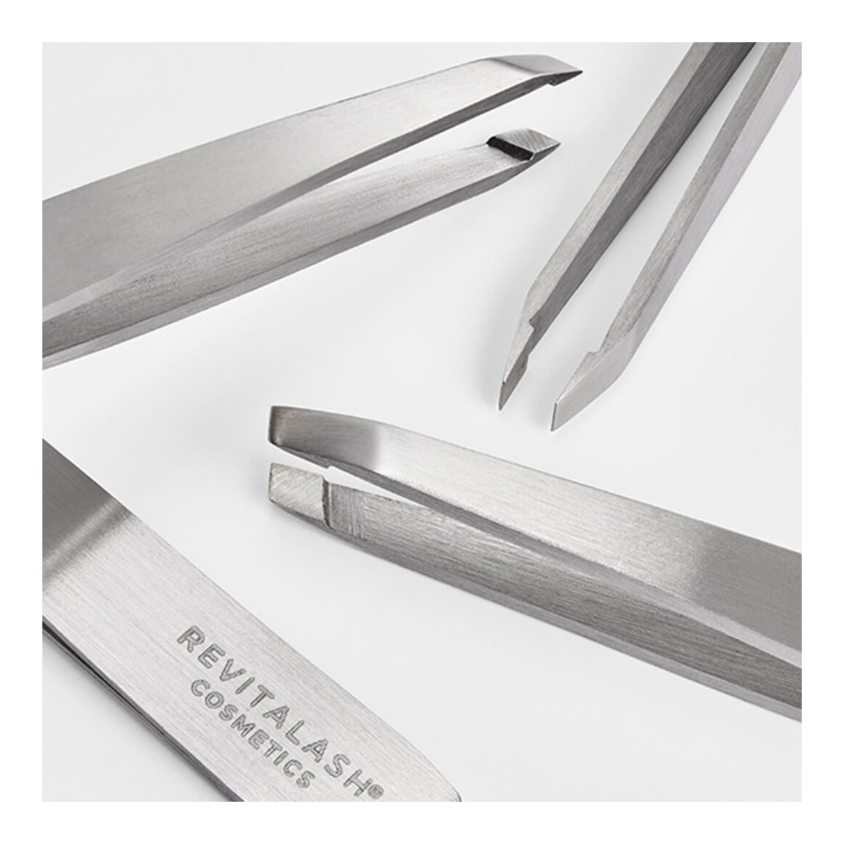 Close-up of four professional-grade RevitaLash Precision Tweezers, made of stainless steel on a white surface, featuring precision tip designs such as slanted and pointed. One tweezer is engraved with RevitaLash.