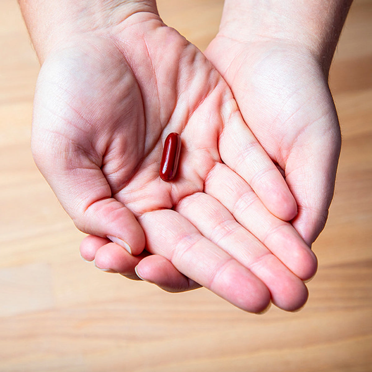 A pair of hands gently cups a red capsule pill, showcasing EyePromise DVS Eye Vitamin for vision support. The pills importance in retinal health, especially for diabetic retinopathy, is highlighted against a light wooden background.