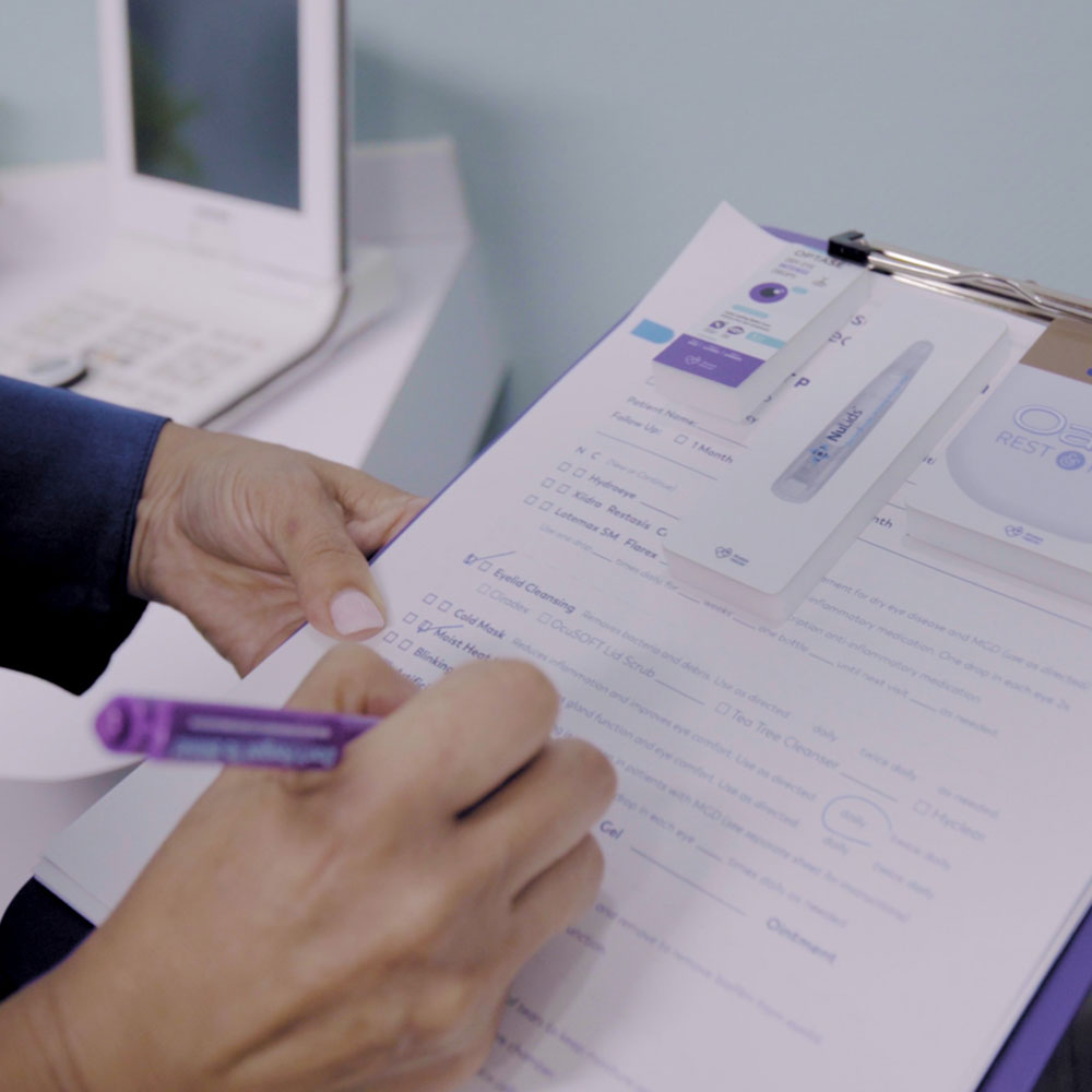 In an exam room, a person uses a purple pen to fill out a form on a clipboard that holds a diagnostic testing device package. Nearby, beneath the soft light streaming through the window, sits a phone and DryEye Rescue’s PKG: Wall Mount Exam Room Display Conversation Starter (Small).