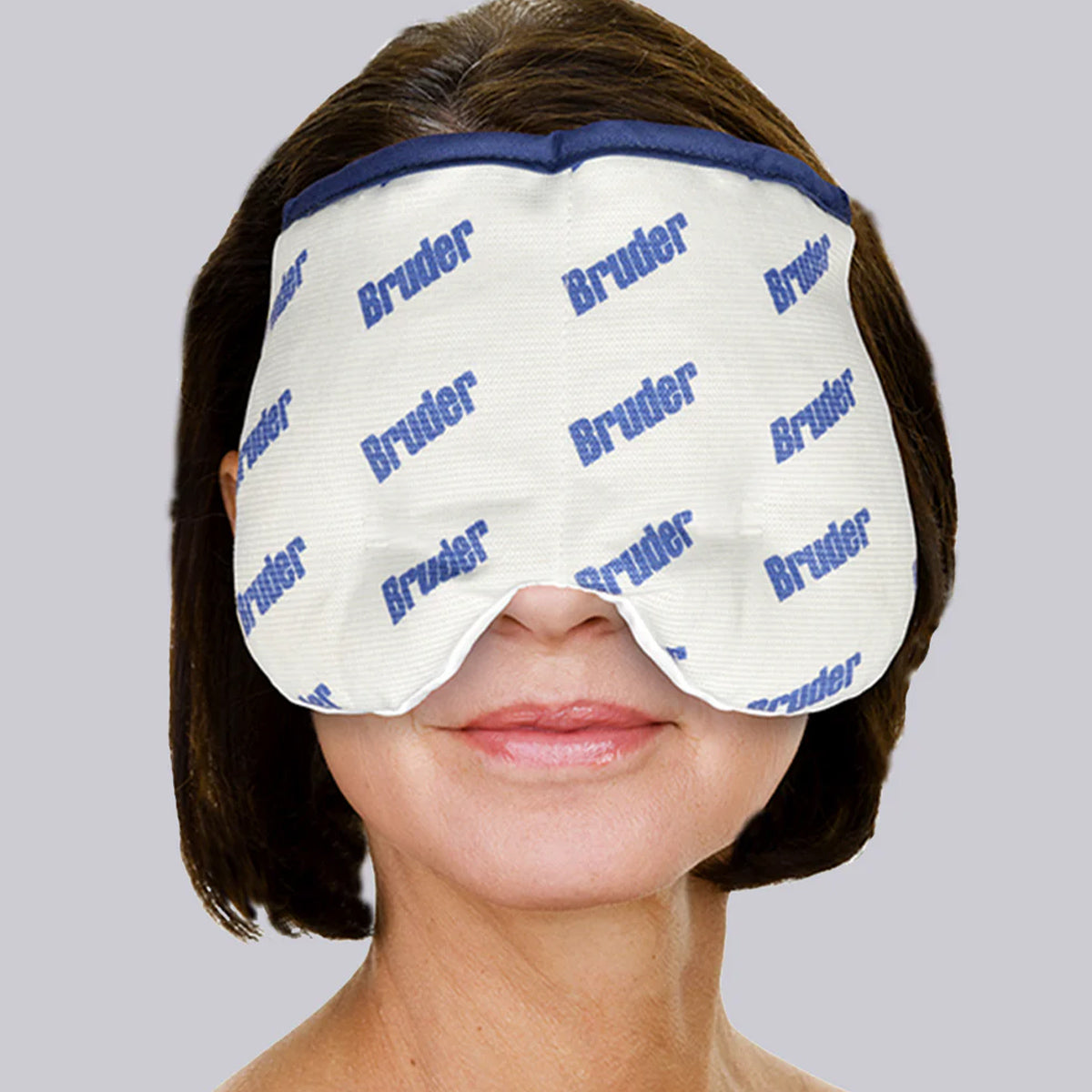 A woman with shoulder-length brown hair wears the Bruder Moist Heat Sinus Compress, a white mask featuring blue Bruder text. It provides soothing sinus relief as it covers her eyes and part of her nose. The background is light gray.