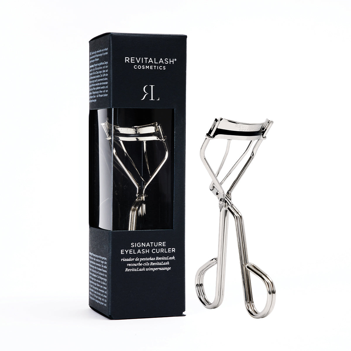 The RevitaLash Signature Eyelash Curler, crafted from carbon steel with silicone pads, is elegantly showcased next to its sleek black packaging, featuring branding and product details. The curler has a shiny finish and ergonomic handles for precision.