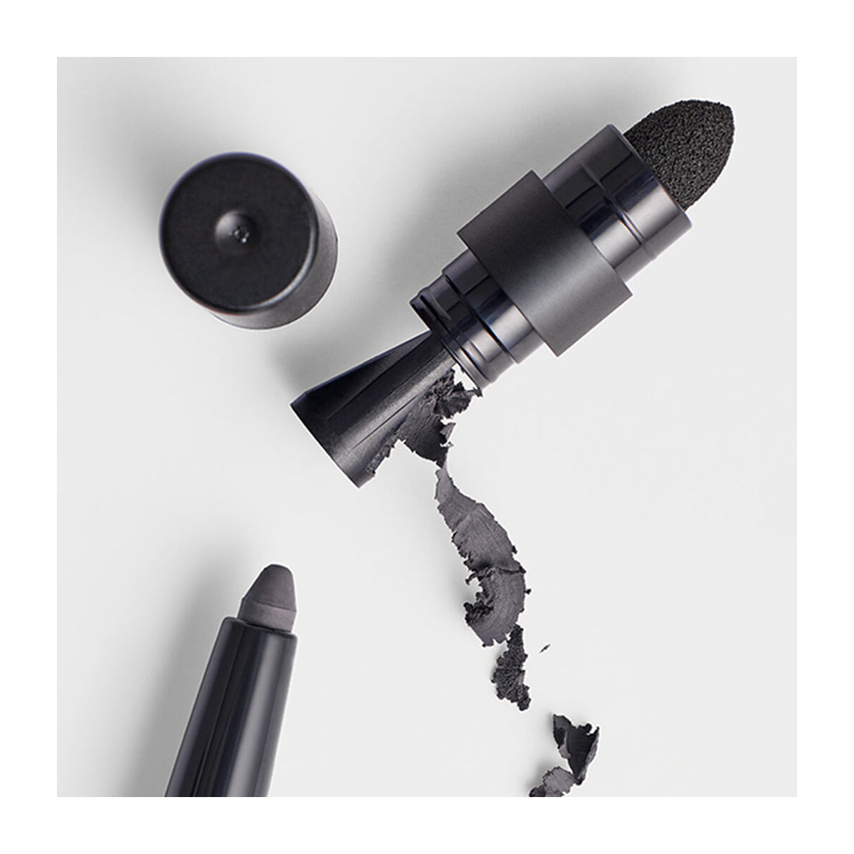 The RevitaLash Defining Liner Eyeliner and its cap rest on a white surface, accompanied by another black makeup tool, suggesting artistry. Black residue hints at the smudge-proof quality of these RevitaLash products.